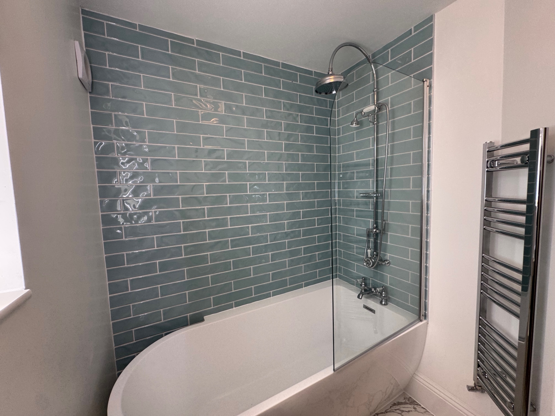 Bathroom detail showing tiled shower wall, glass screen and heated towel rail