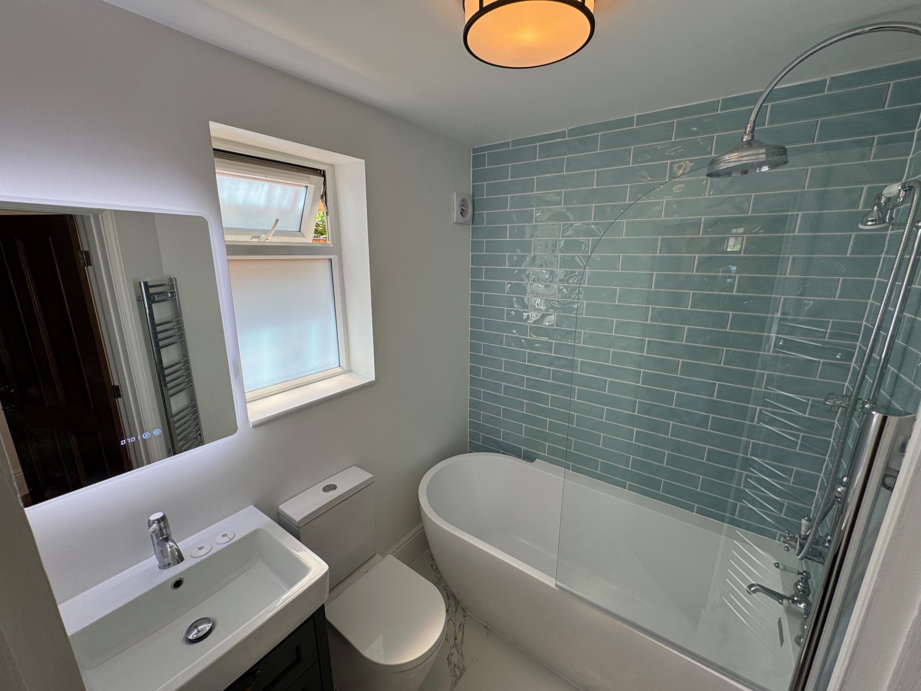 New bathroom with green metro tiling, bath, shower and wall-hung basin