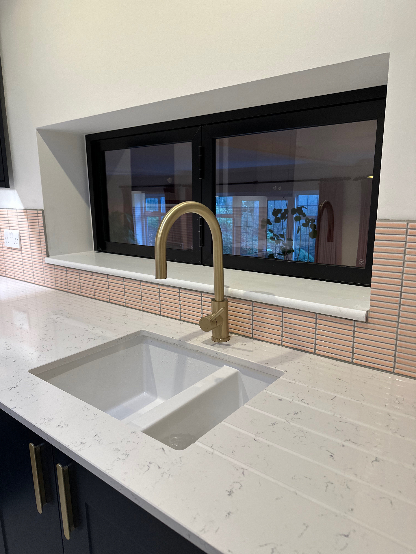 Brass kitchen tap and undermount sink set into the pale worktop before the black-framed internal window