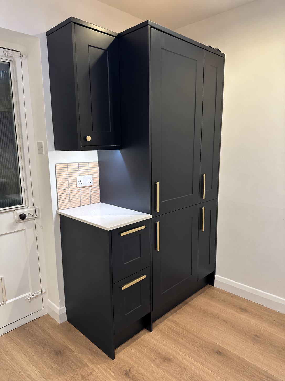 Floor-to-ceiling dark shaker tall cabinetry with brass handles beside the kitchen door