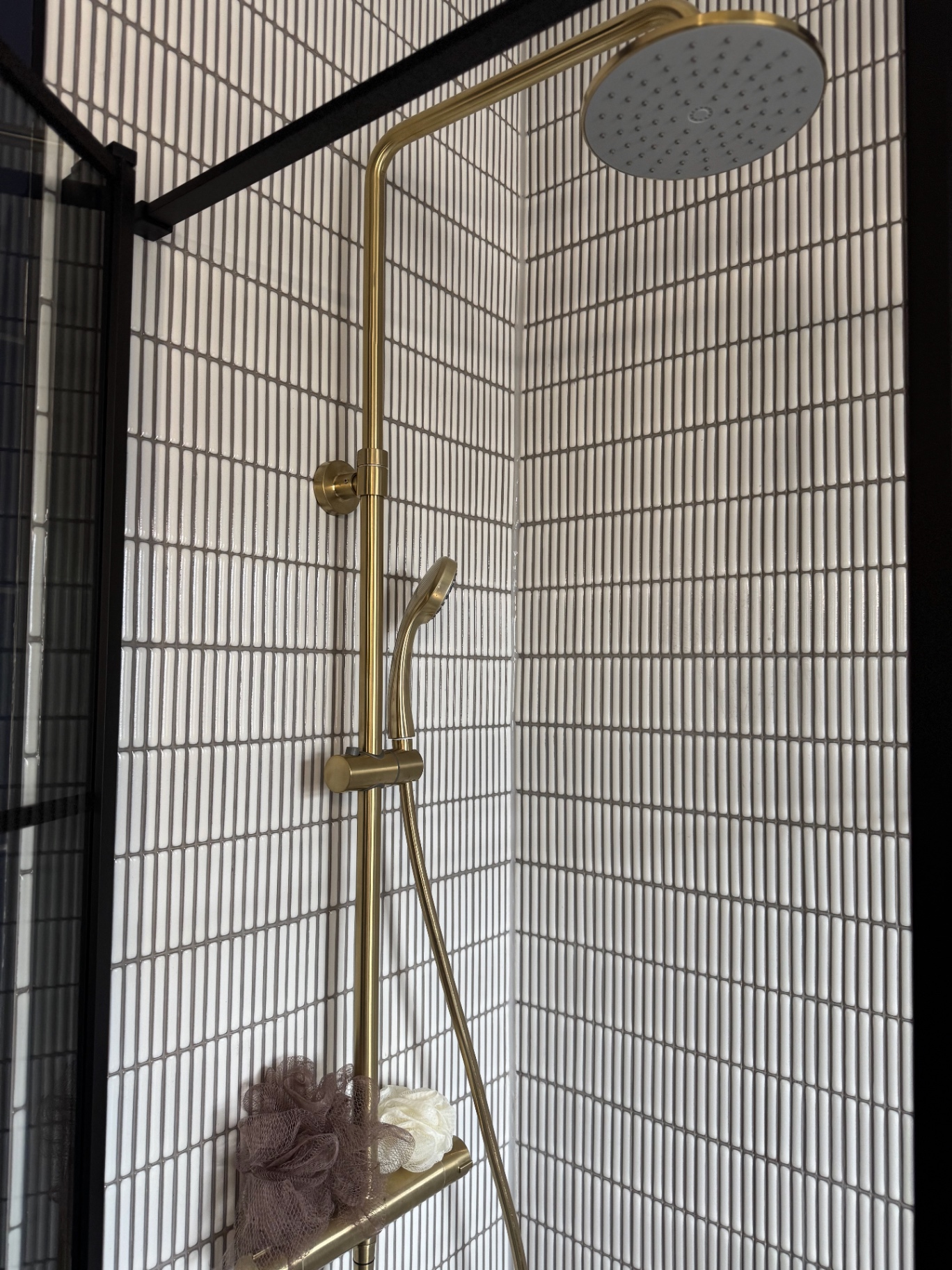 Brushed brass shower system with rainfall head and hand shower against white feature tiling