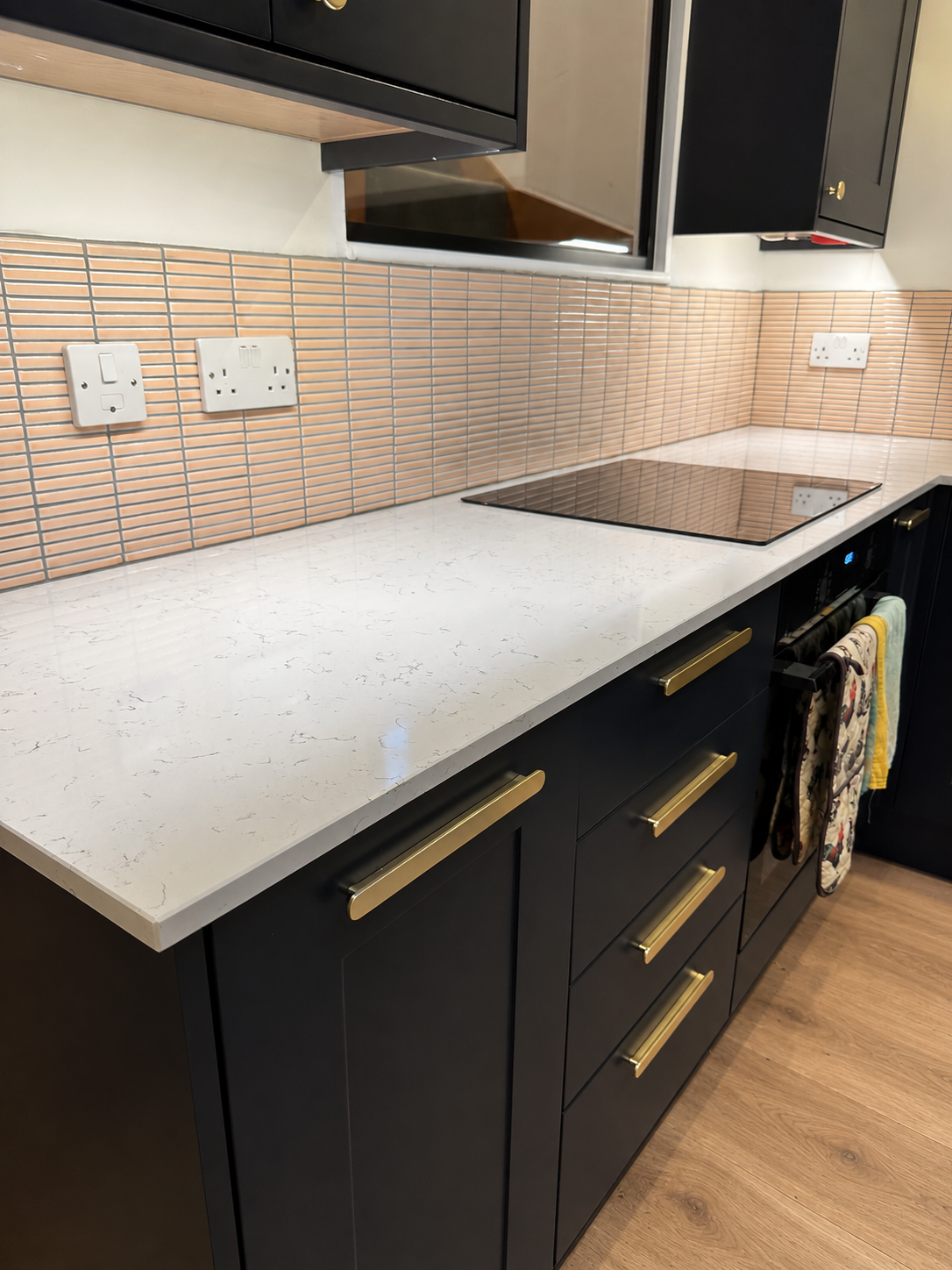 Pale worktop run with brass bar handles, induction hob and peach-toned tiled splashback