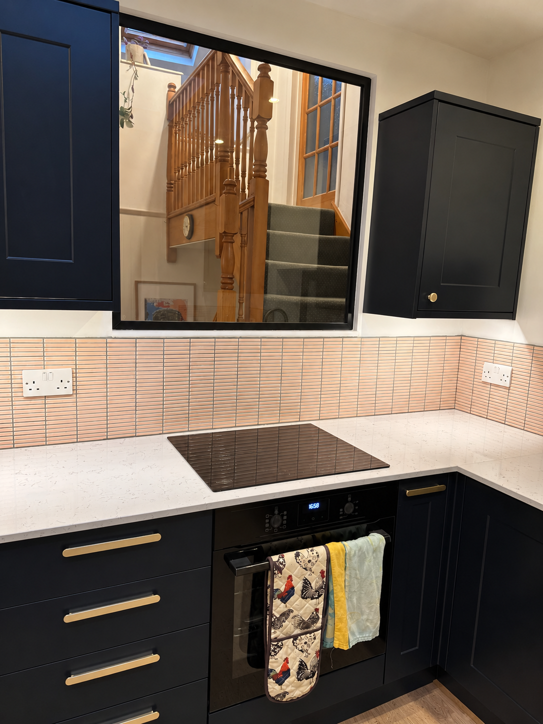 Induction hob and built-in oven beneath the black-framed internal window looking onto the staircase