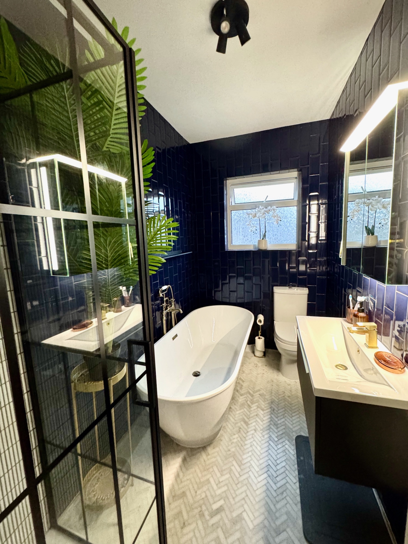 Finished Earlswood bathroom with navy tiling, freestanding bath, brass fittings and black-framed walk-in shower