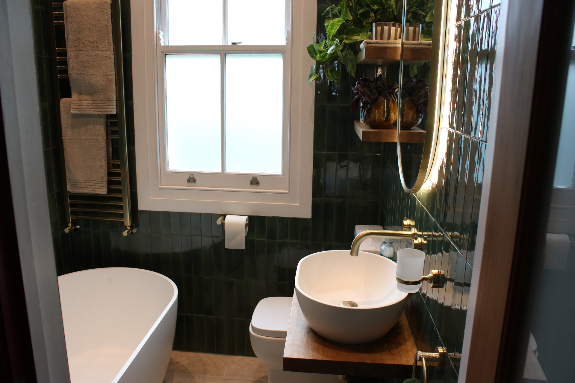 Wide view of the completed bathroom showing the freestanding bath, brass towel radiator and green tiled walls