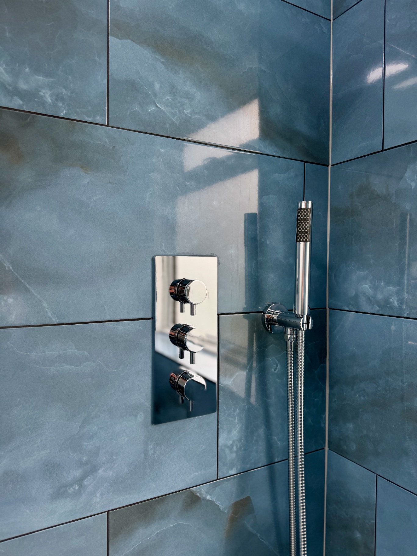 Close-up of the concealed chrome shower controls and hand shower against blue porcelain tiling