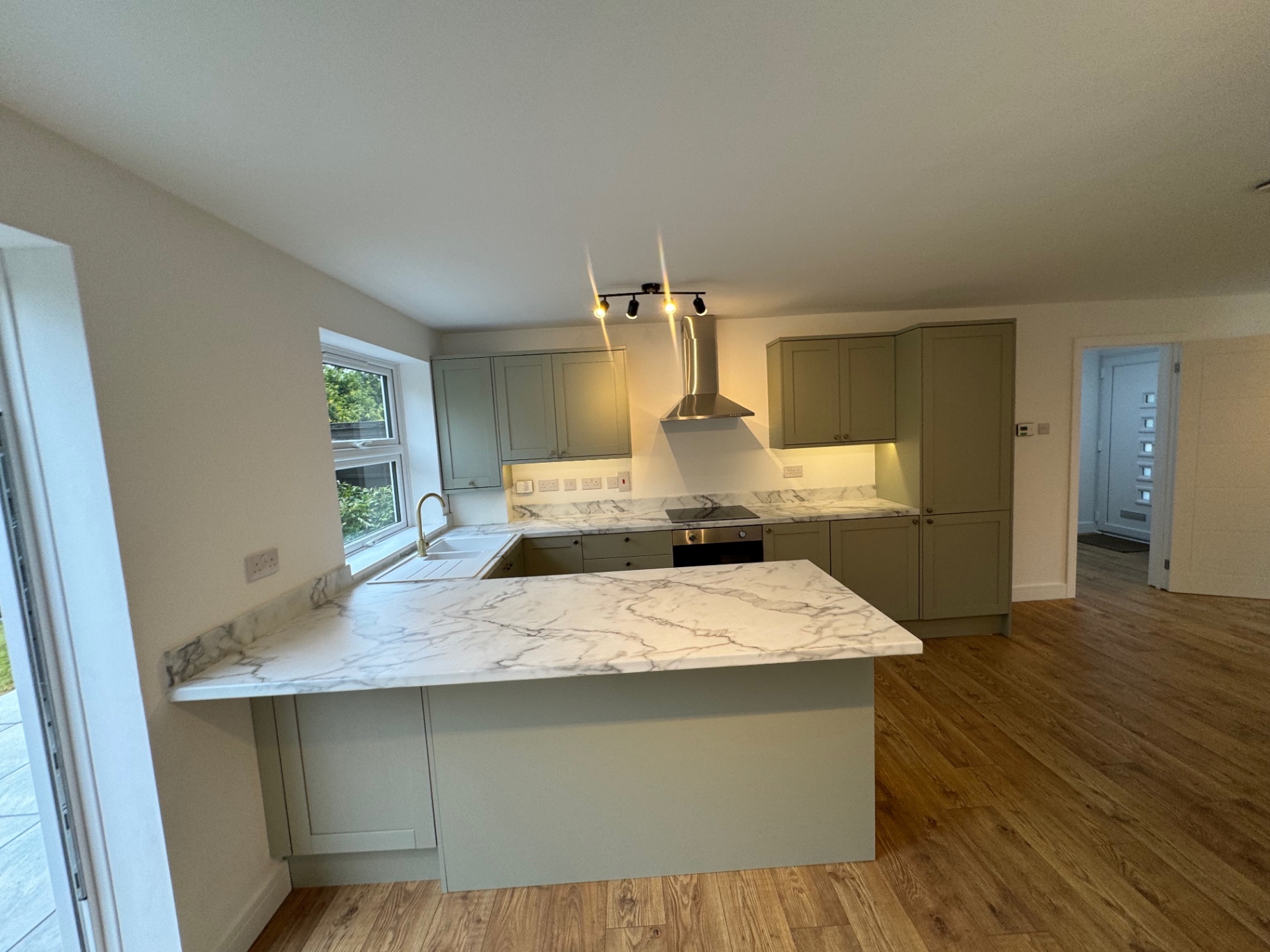 Marble-effect peninsula worktop with sage cabinetry and extractor beyond