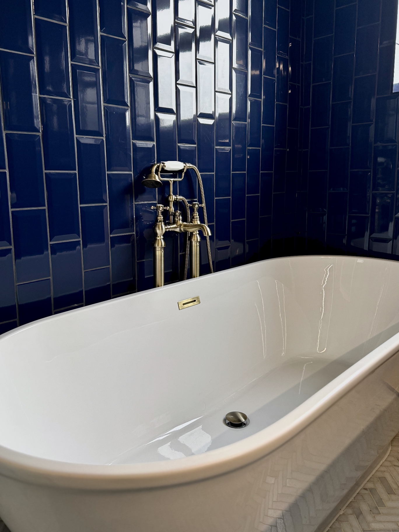Close-up of the freestanding bath rim with brushed brass floor-mounted tap and handheld shower