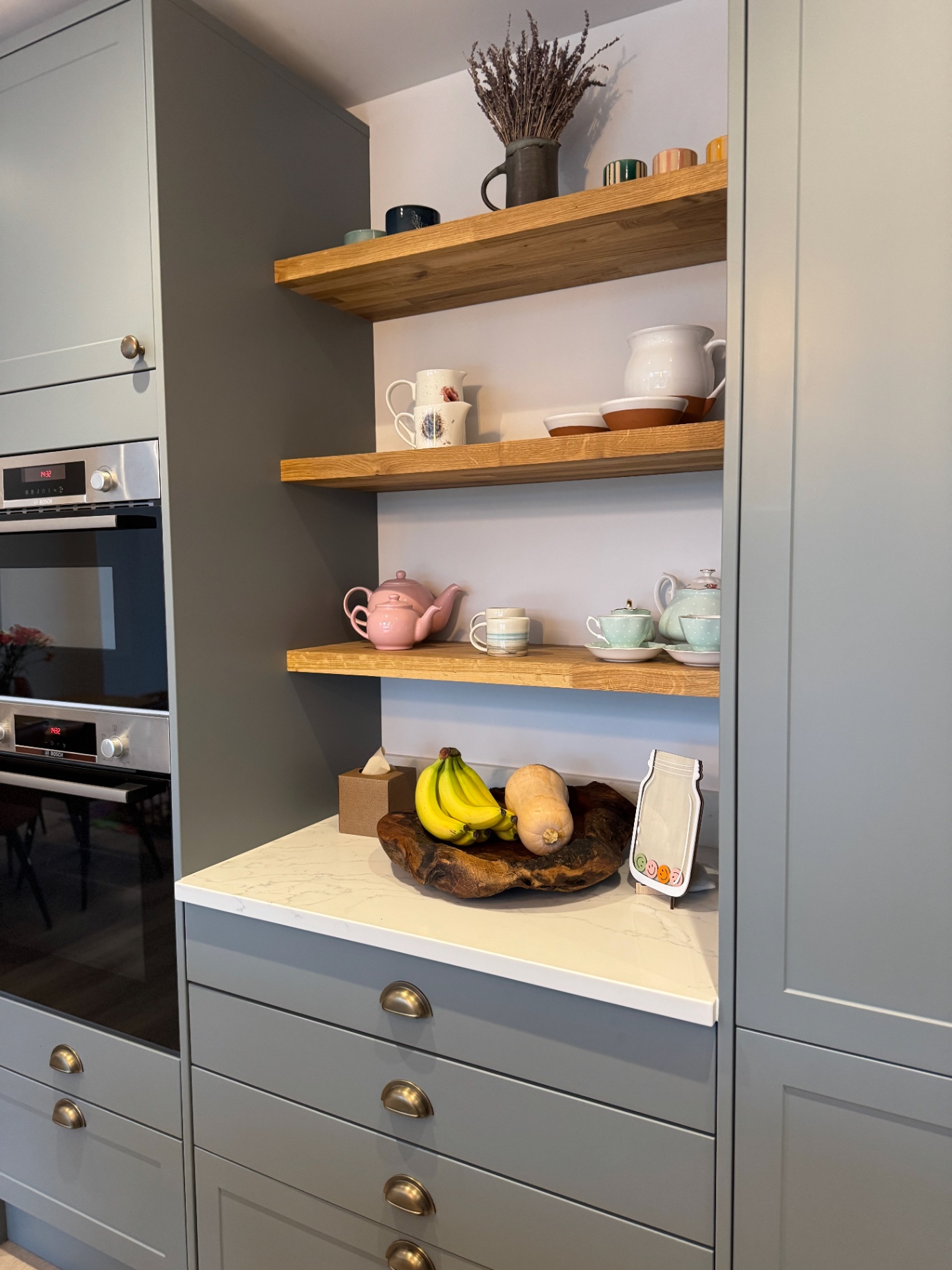 Oak shelving set between full-height grey cabinetry and built-in ovens
