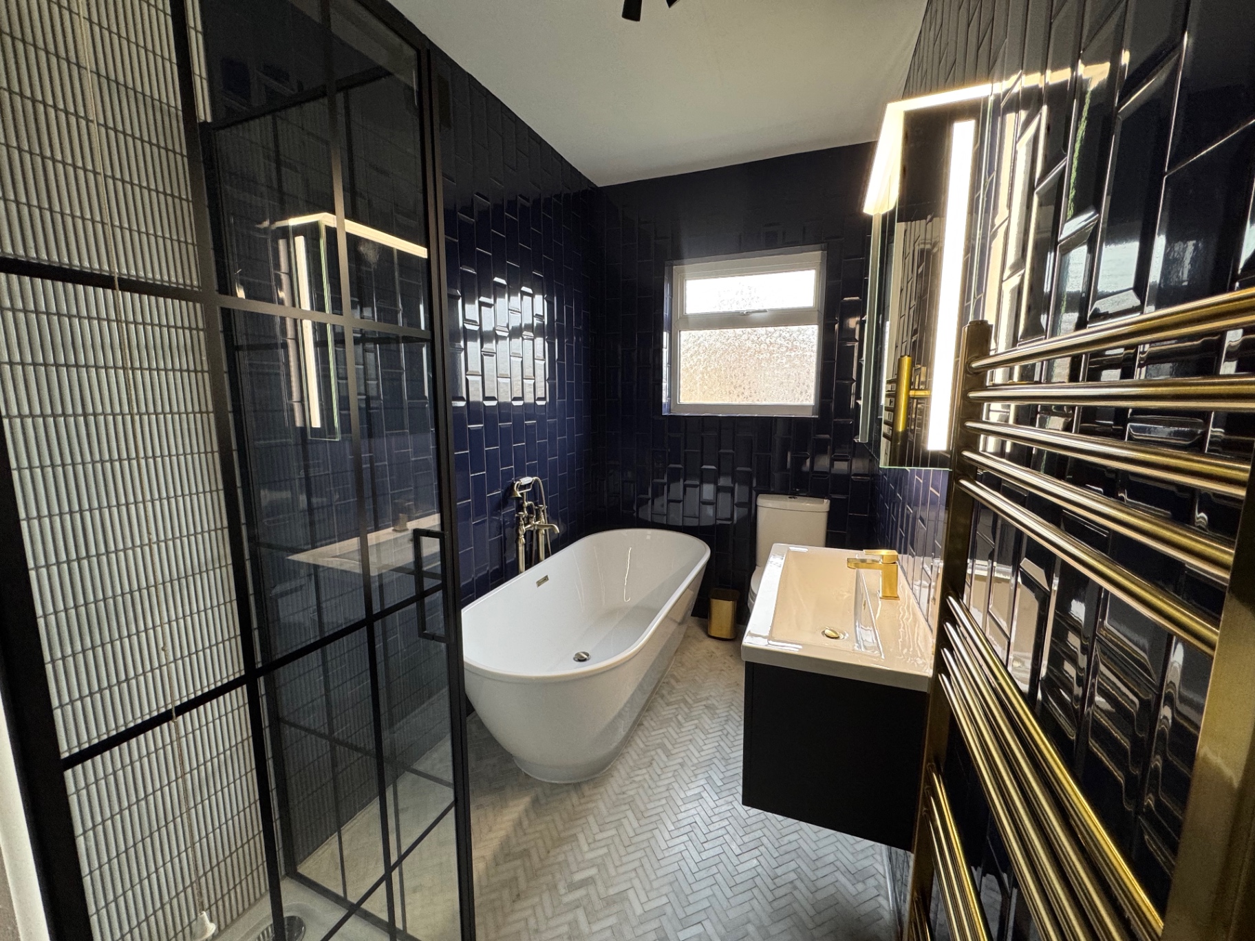 Earlswood Bathroom Full view of the finished Earlswood bathroom with navy wall tiles, freestanding bath, black-framed shower and brass fittings