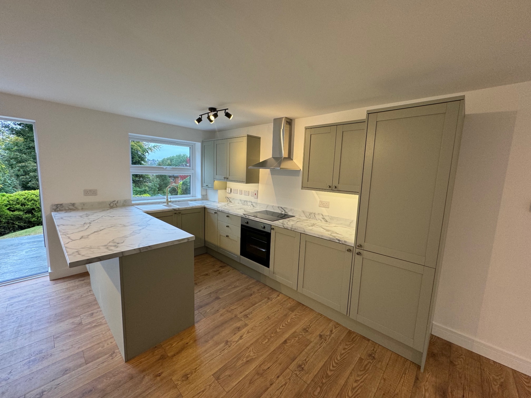 Wide view of the completed sage shaker kitchen with peninsula and full-height cabinetry