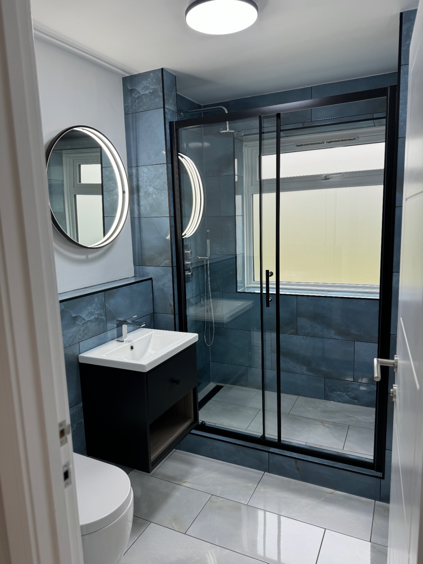 Blue Porcelain Walk-In Shower, Cordrey Gardens Contemporary bathroom with blue porcelain tiling, black-framed walk-in shower and illuminated round mirror
