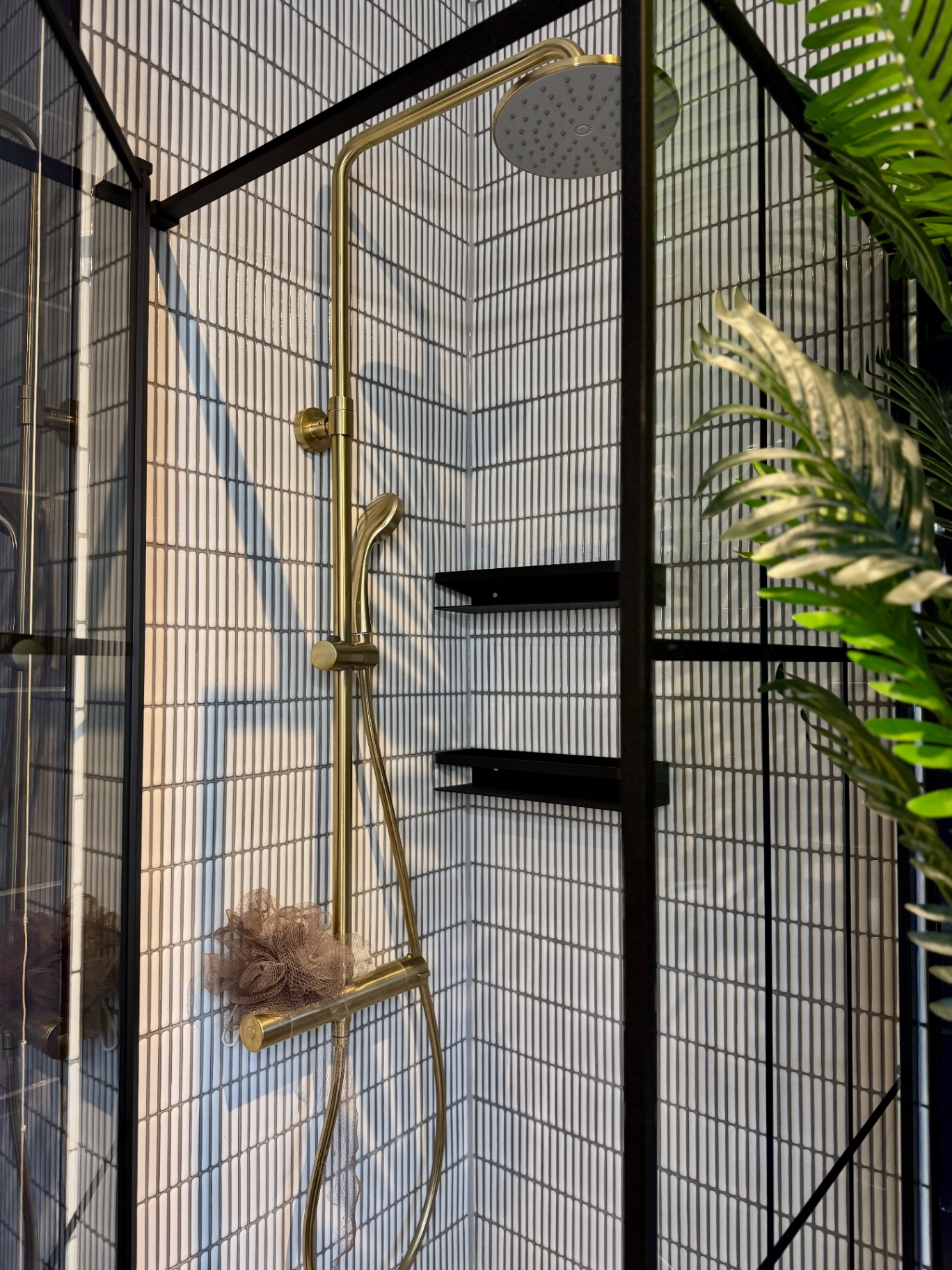 Walk-in shower corner with matte black recessed shelves, black-framed glazing and white tiled walls