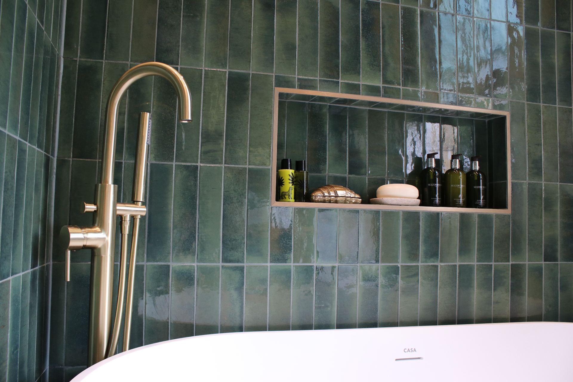 Freestanding bath with brushed brass floor-mounted taps against deep green wall tiling