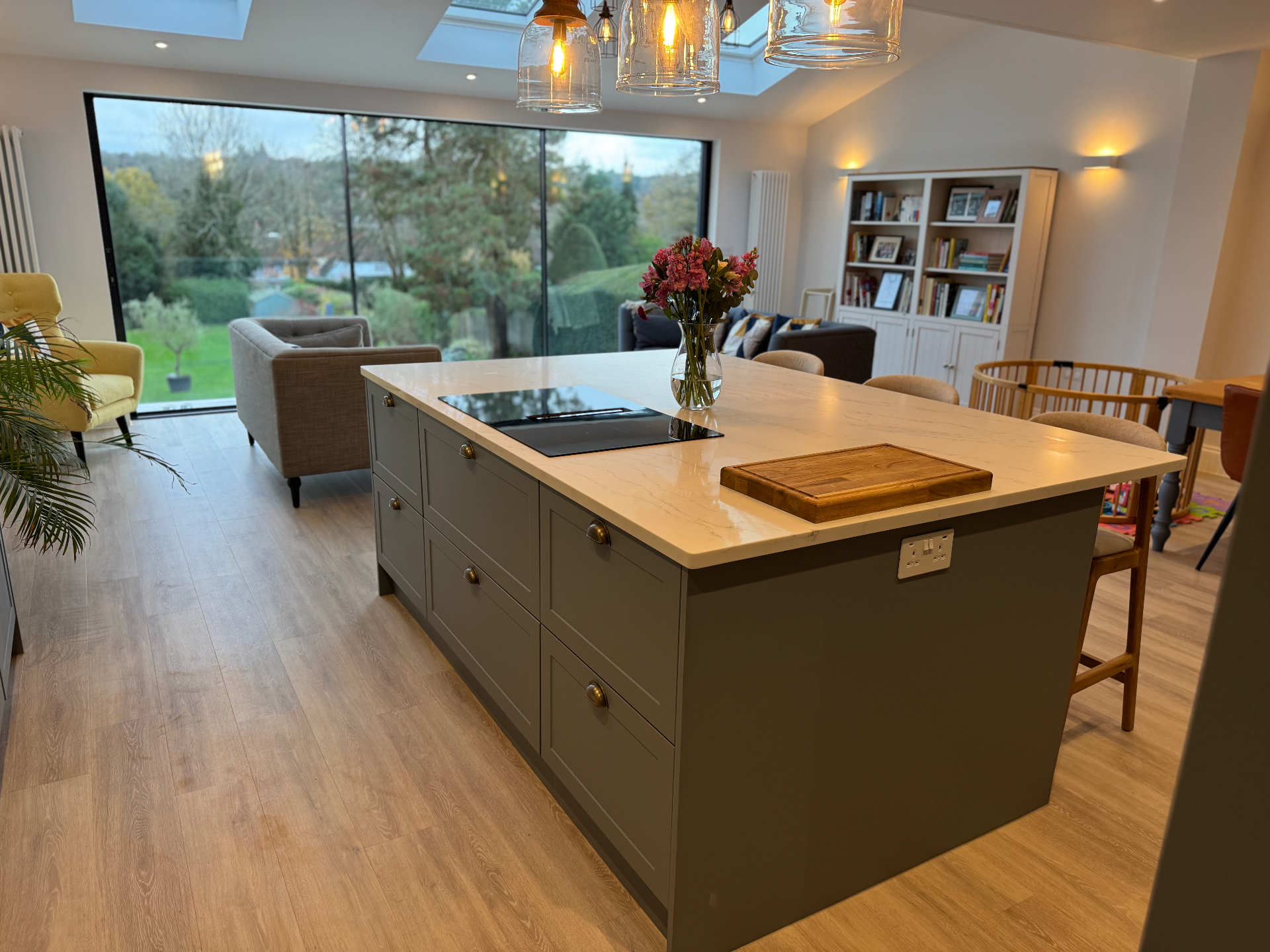 Open-plan kitchen and living space with the island in the foreground, looking towards the garden through full-height glazing
