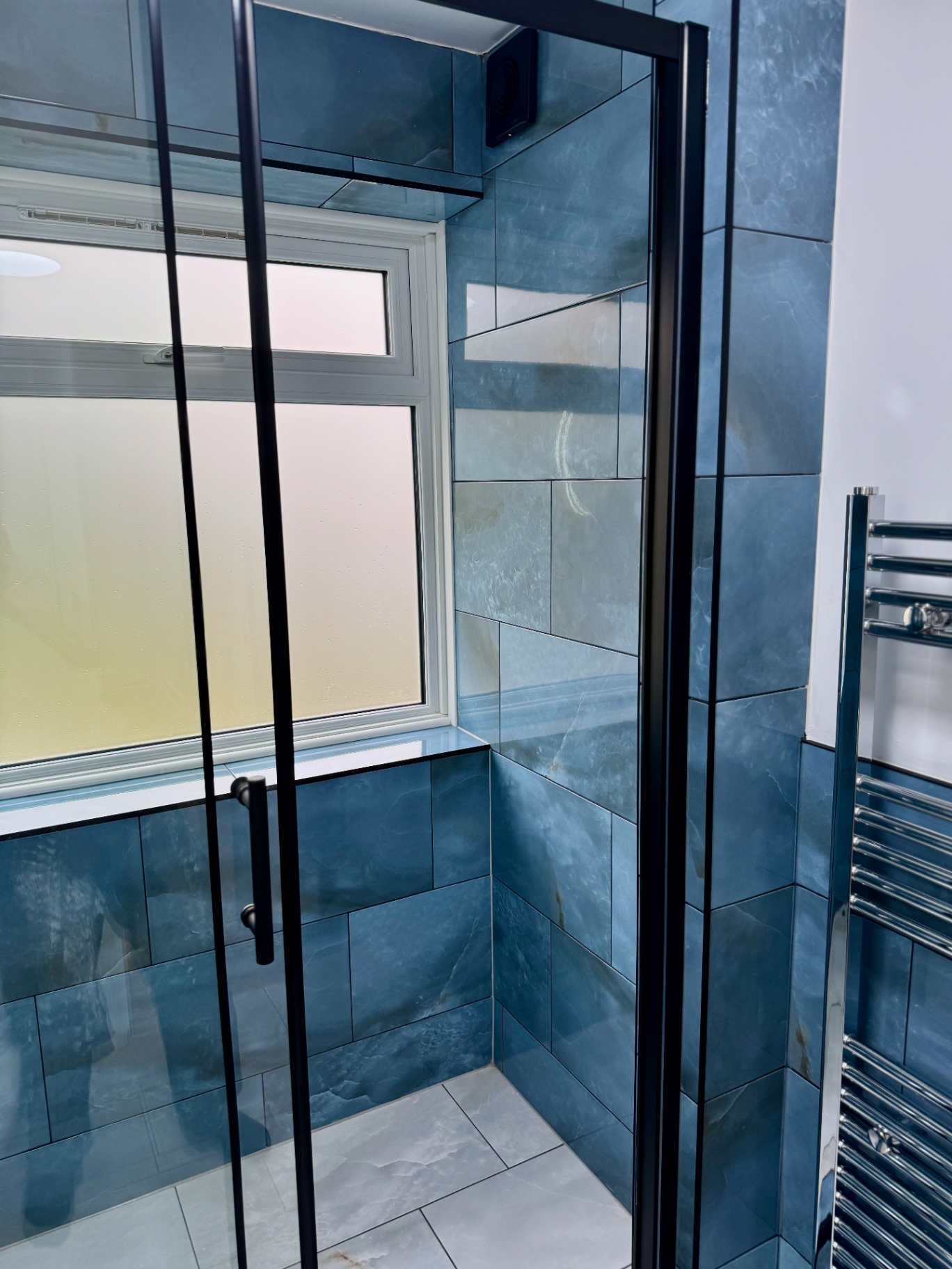 Black-framed shower glazing with tiled window reveals and chrome heated towel rail