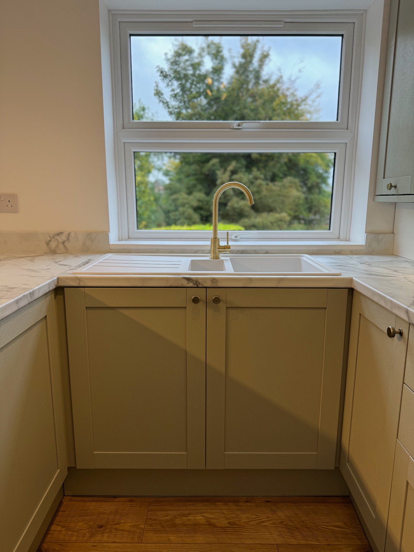 Ceramic sink and brass tap set beneath the kitchen window
